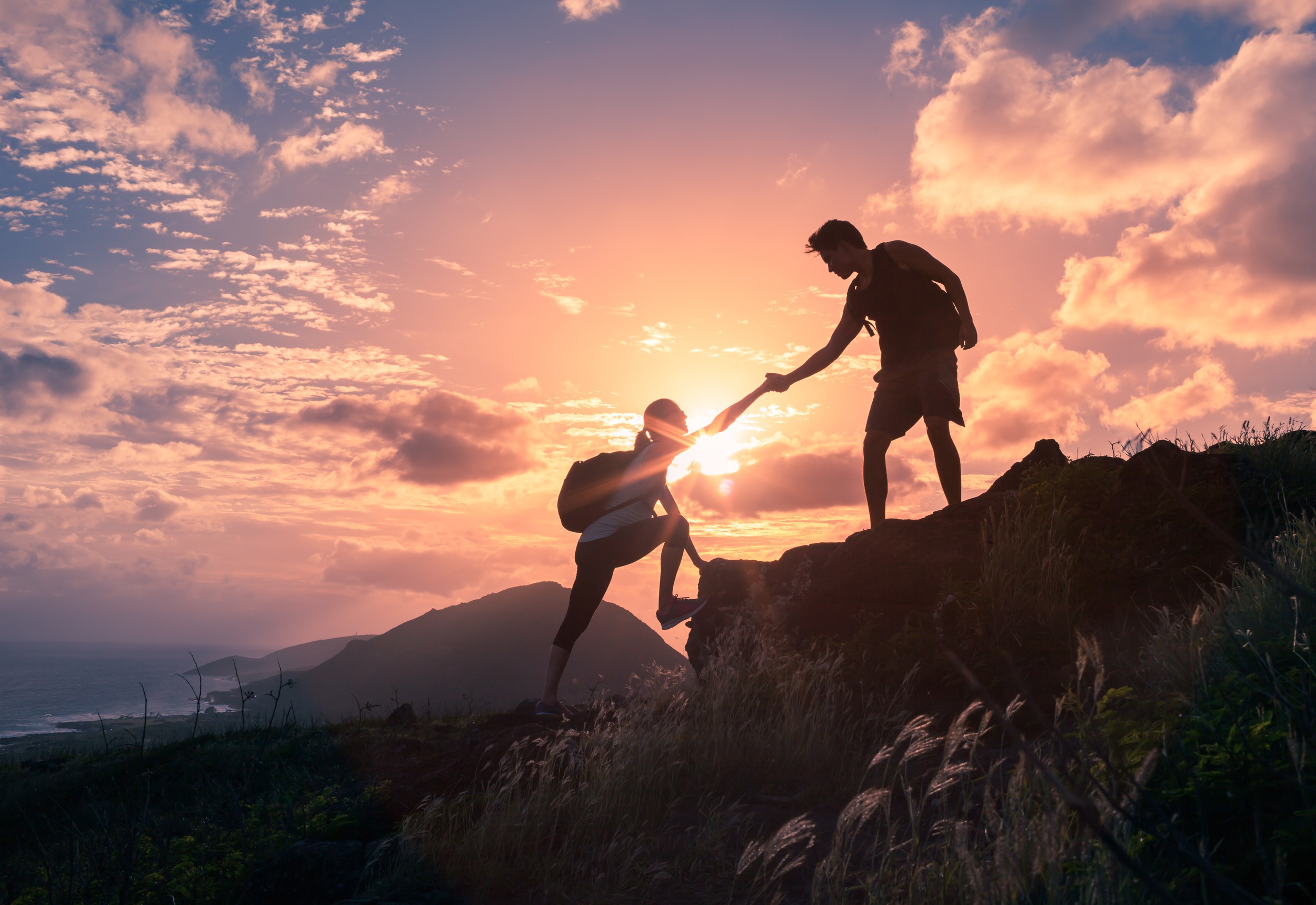 People helping each other hike up a mountain at sunrise.